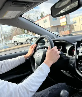 Over-the-shoulder view of a learner steering during a behind-the-wheel lesson