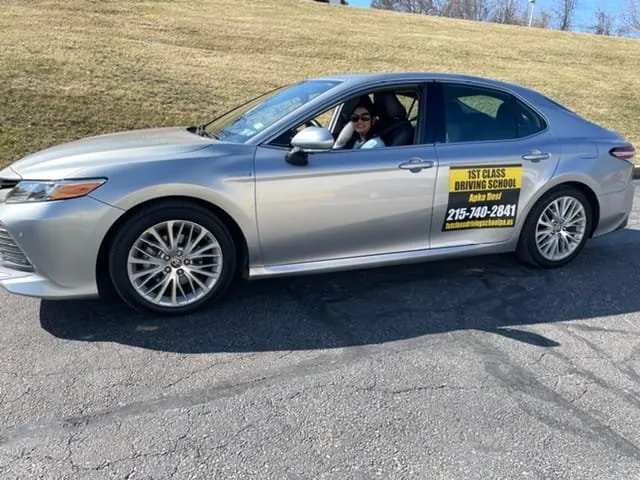 Silver dual-control training car with 1st Class Driving School door signage, instructor at the wheel