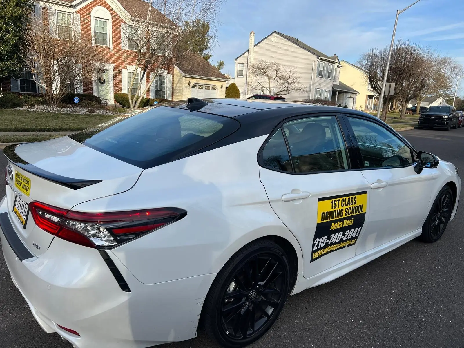 White training car at the curb on a residential street used for early lessons