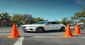 A white sedan perfectly parallel parked within the 24x8 foot parallel parking test dimensions in Pennsylvania, marked by orange traffic cones on a suburban street.