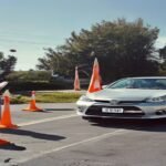 A student driver practicing the parallel parking test rules in PA between orange cones and a concrete curb